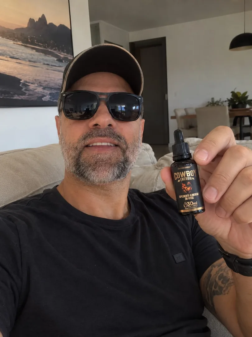 Homem de boné e óculos escuros no sofá, segurando um frasco COWBOY Energia