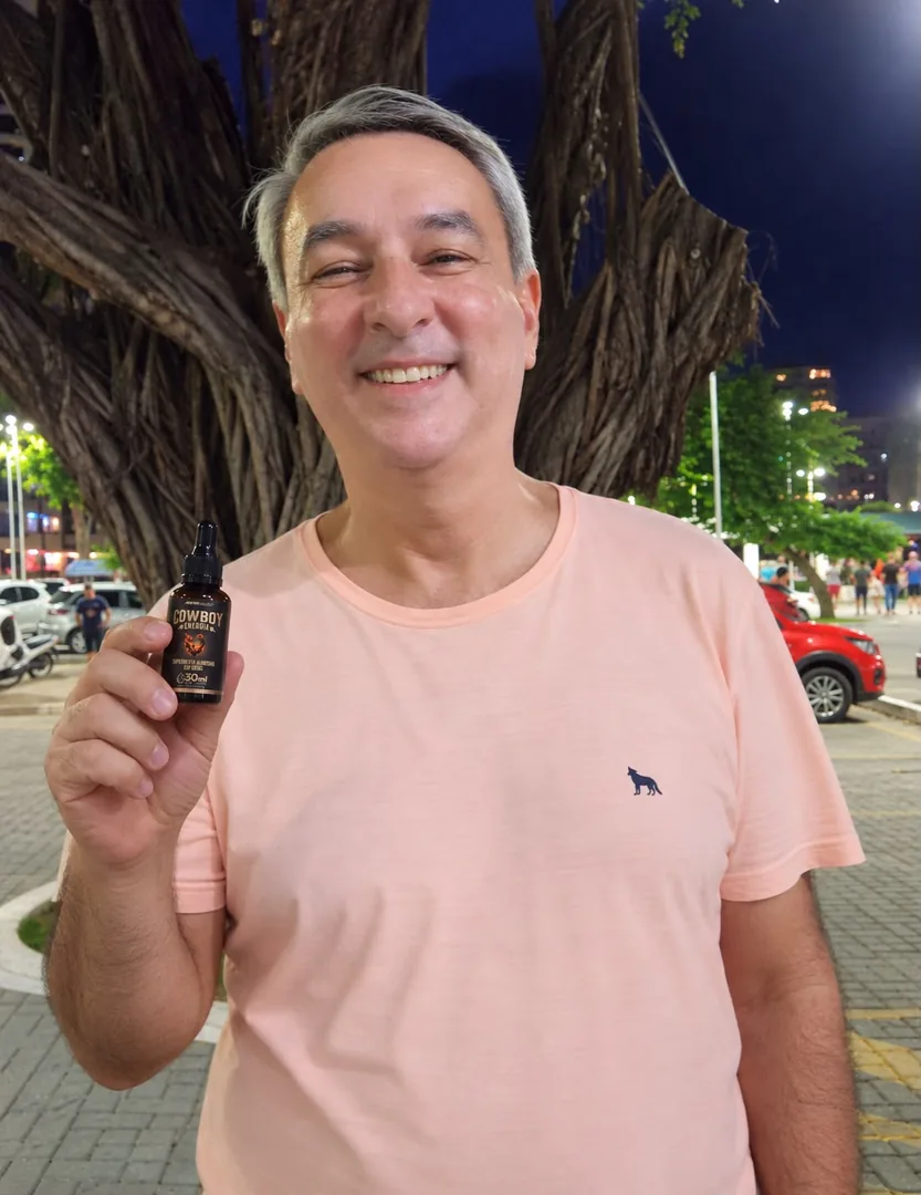 Homem de camisa clara sorrindo em uma praça à noite, segurando um frasco COWBOY Energia
